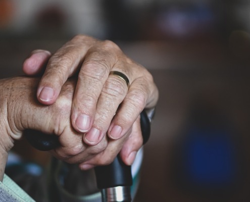 The hands of an older adult holding the top of a cane.