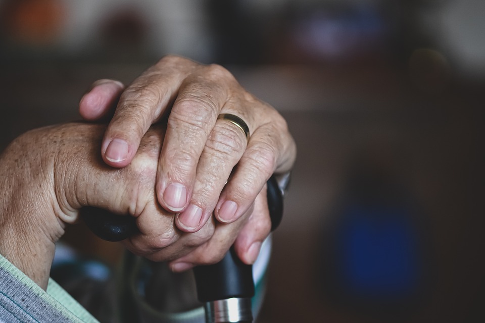 The hands of an older adult holding the top of a cane.