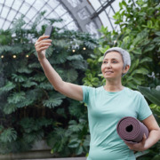 An older adult holding a yoga mat and looking at a smartphone.